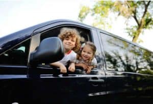 2 kids poking their heads out of a black minivan which is filled with car hacks for moms