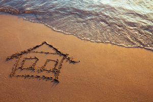 Drawing of a simple house in the sand with water lapping nearby