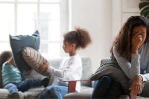 Mom who is tired and want to quit homeschooling with two children pillow fighting in the background.