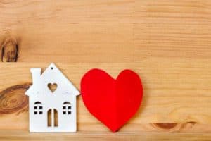 What is a homemaker? Small cutout house with red heart on wooden background