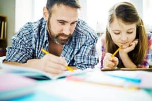 Dad involved in homeschooling his daughter. Both lounging on the floor doing homework.